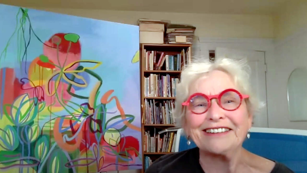 Artist Sas Colby next to her painting, talking on a zoom