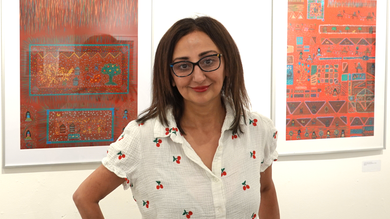 Artist Fedra Yazdi standing before her framed artwork